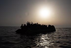 Ein überfülltes Boot mit Flüchtenden auf dem Meer im Gegenlicht.